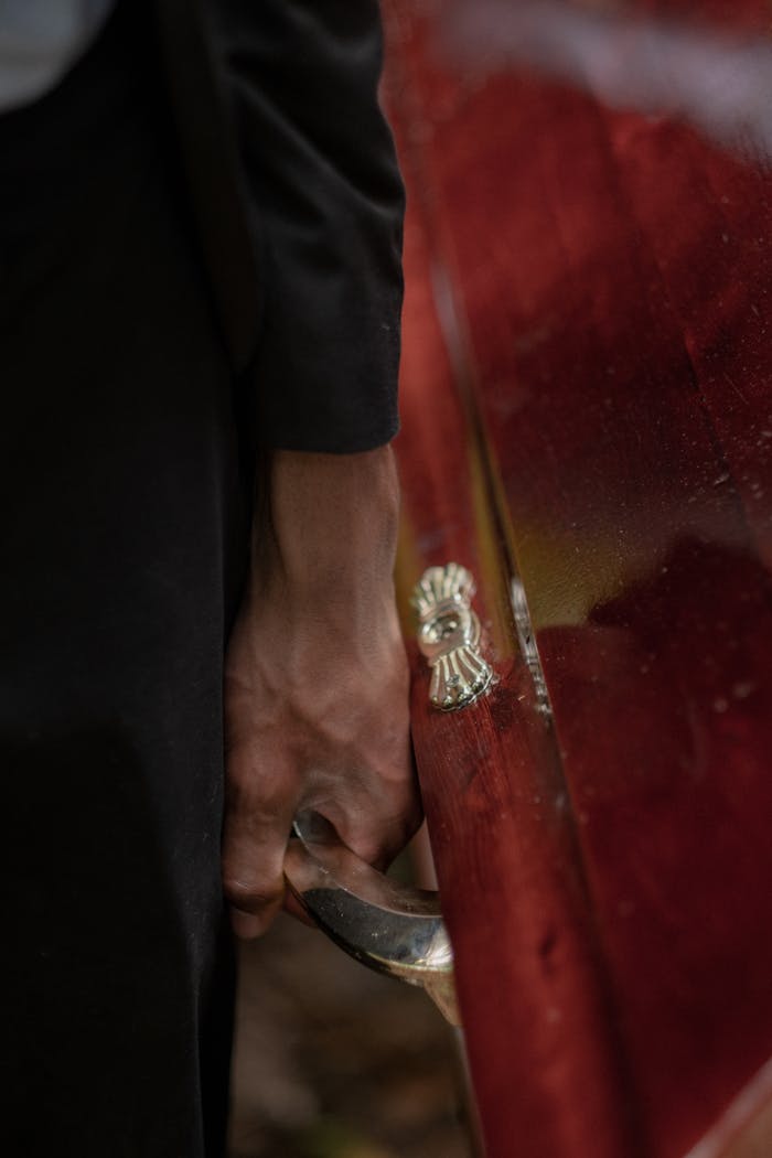 Detail shot of a hand grasping a coffin handle, symbolizing farewell and mourning.